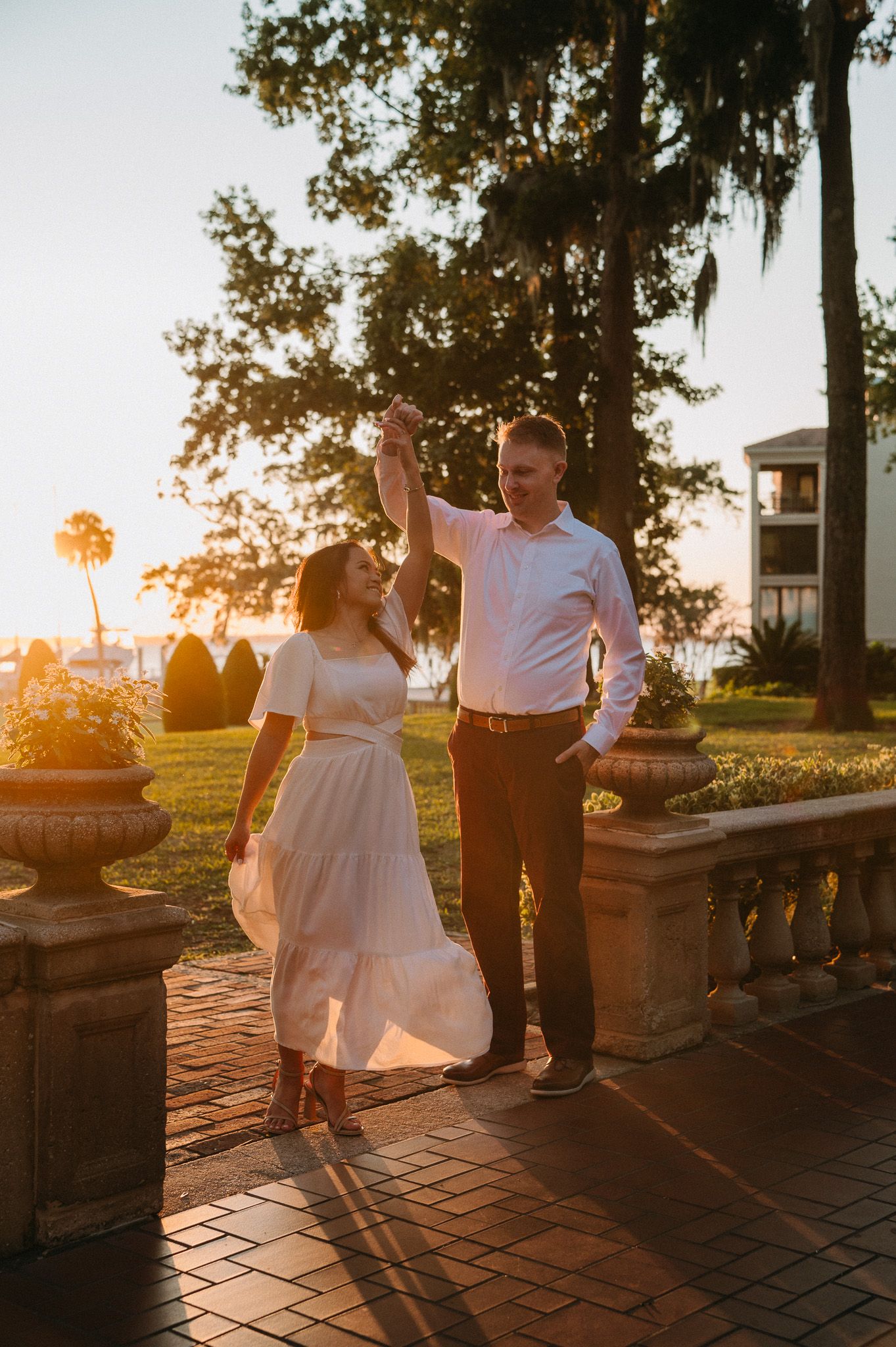 Couple dancing at golden hour on a brick terrace surrounded by palm trees and stone urns.