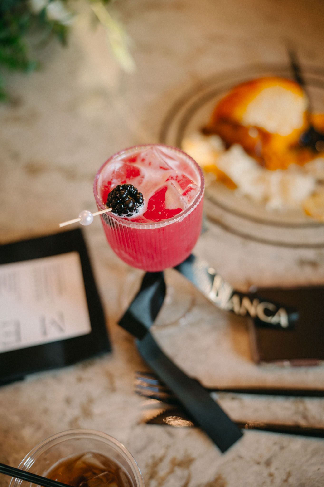 Pink berry cocktail garnished with blackberry on decorative pick at elegant wedding reception table.