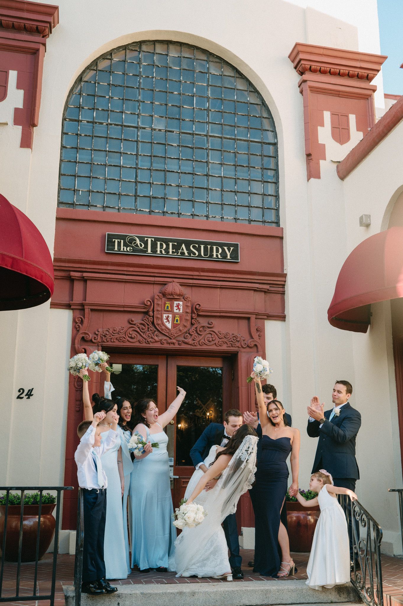 Wedding party celebrating outside The Treasury venue, bride in white gown with veil, bridesmaids in blue and black dresses.