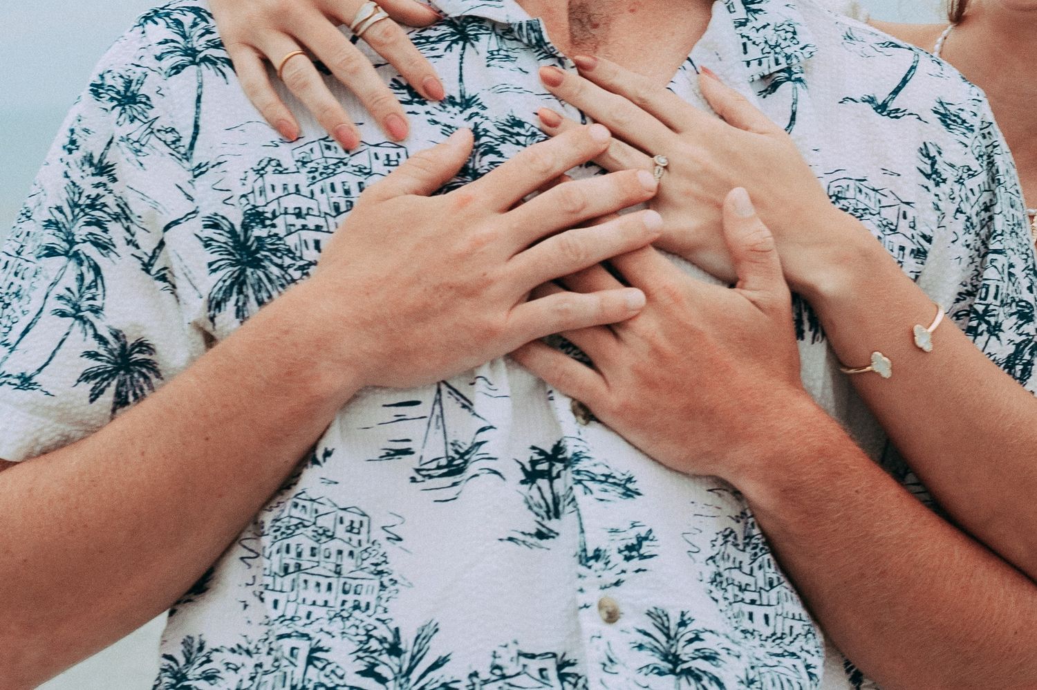 Close-up of a couple's hands placed tenderly on a man's tropical print shirt.