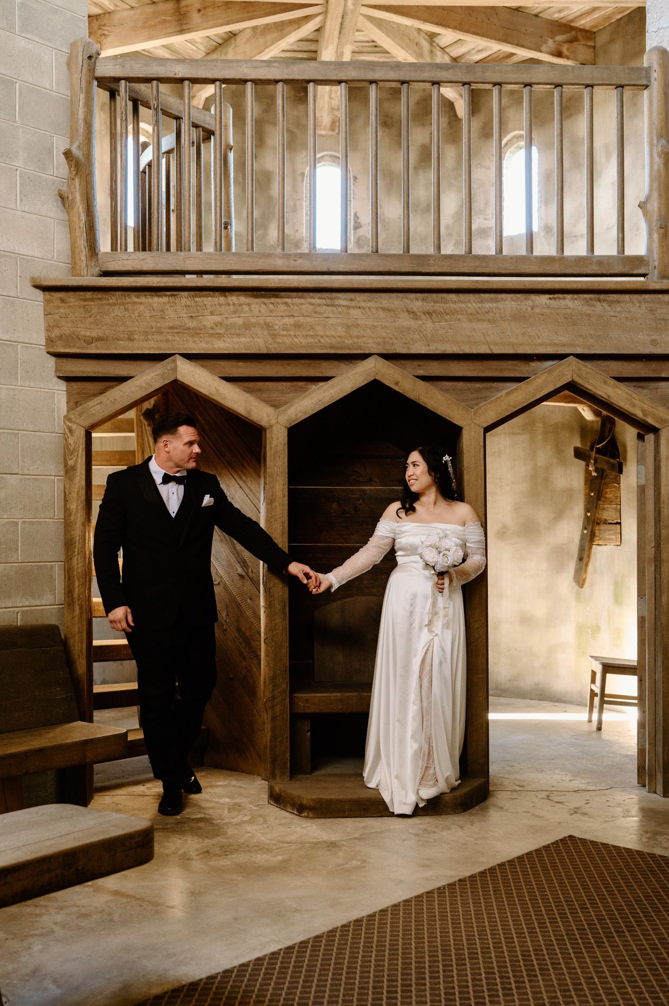 Bride and groom holding hands walking through wooden archway in stone church wedding venue.