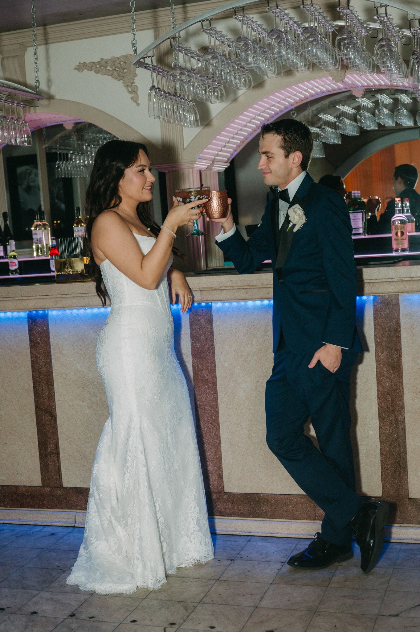 Bride in white gown and groom in navy suit toast drinks at a elegant wedding reception bar.