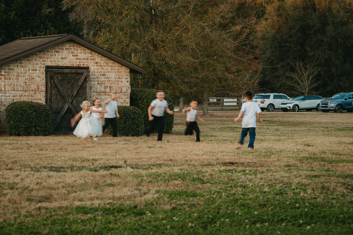 Children running and playing in a grassy field near a stone building at an outdoor wedding.