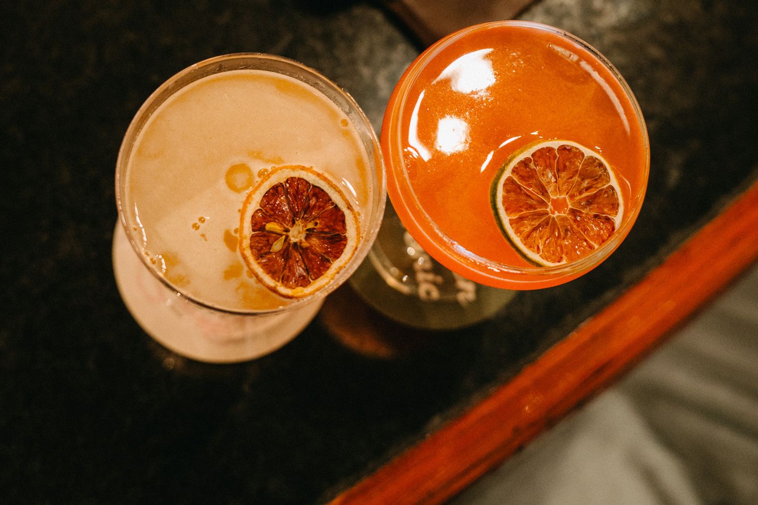 Overhead view of two cocktails garnished with dried blood orange slices on dark surface.
