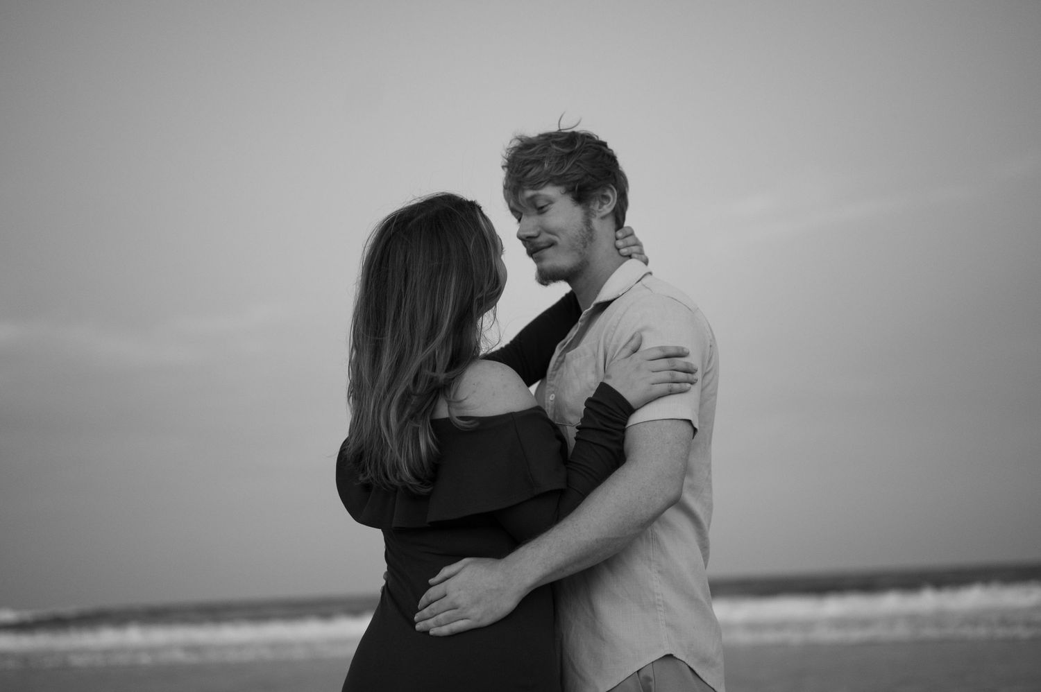 Black and white photo of a young couple embracing romantically on a beach.