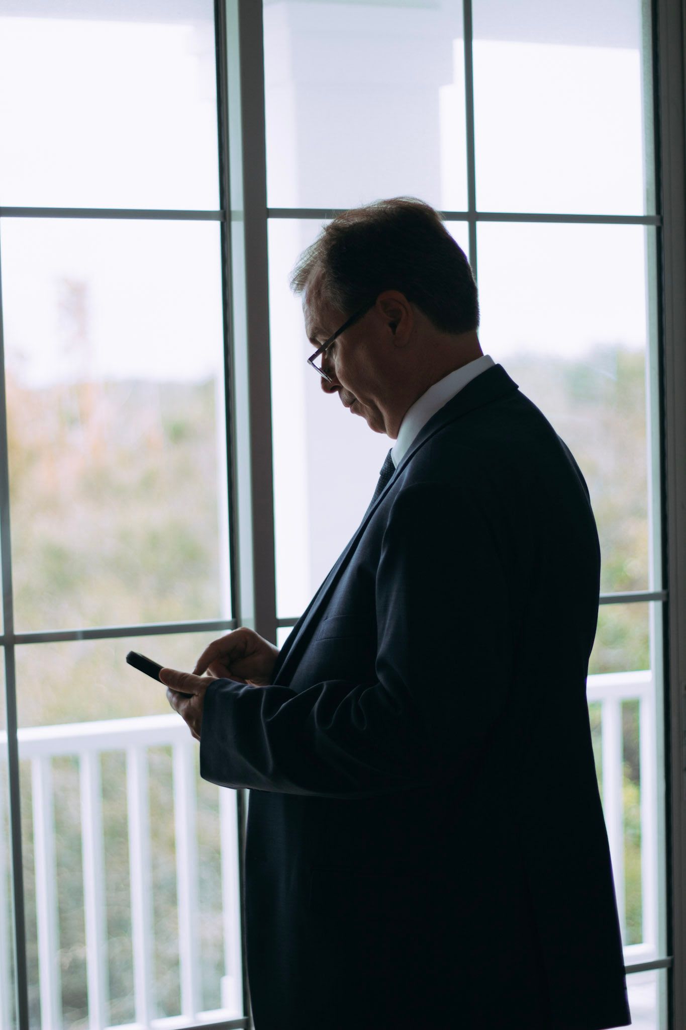 Businessman in dark suit checking smartphone by large window with natural light.