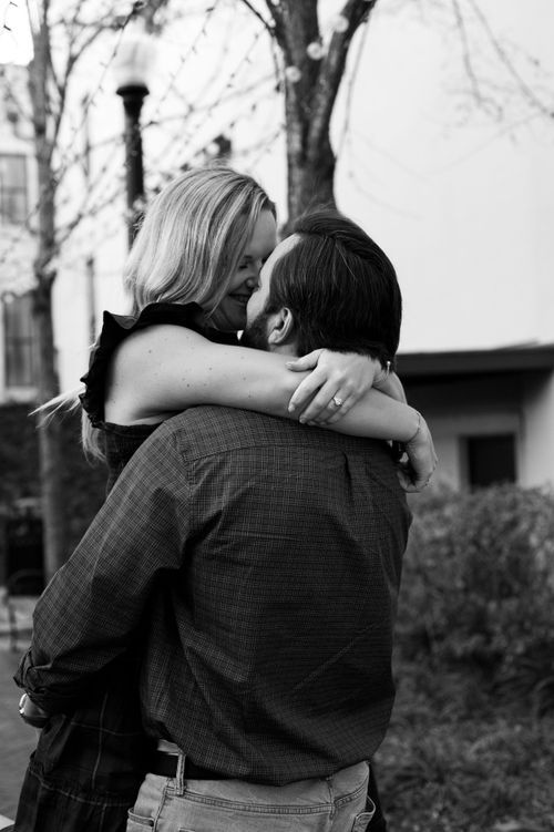 Couple sharing tender embrace outdoors in black and white engagement photo.
