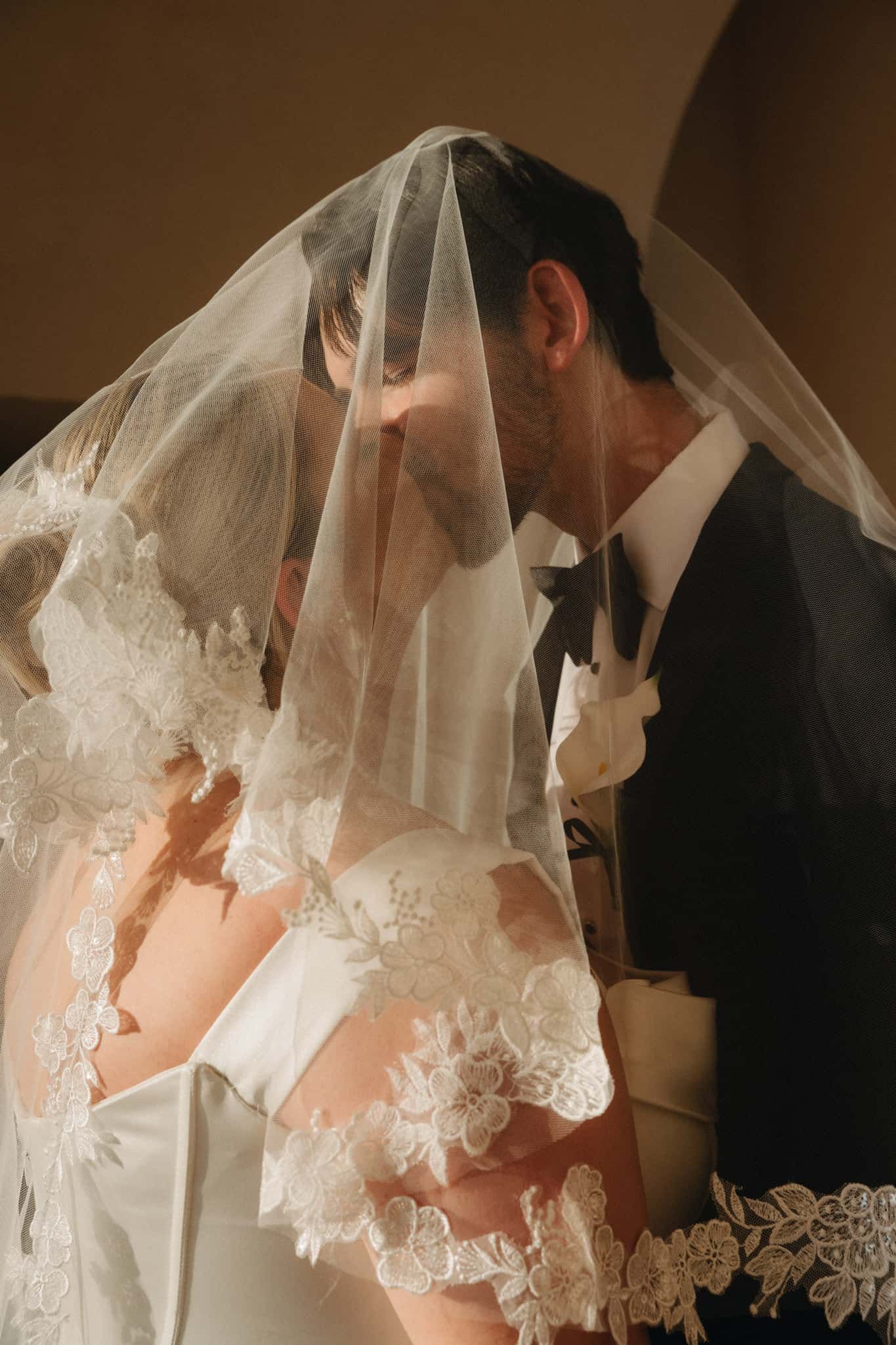Bride and groom sharing a romantic kiss under a lace-trimmed wedding veil during their ceremony in St. Augustine, Florida.
