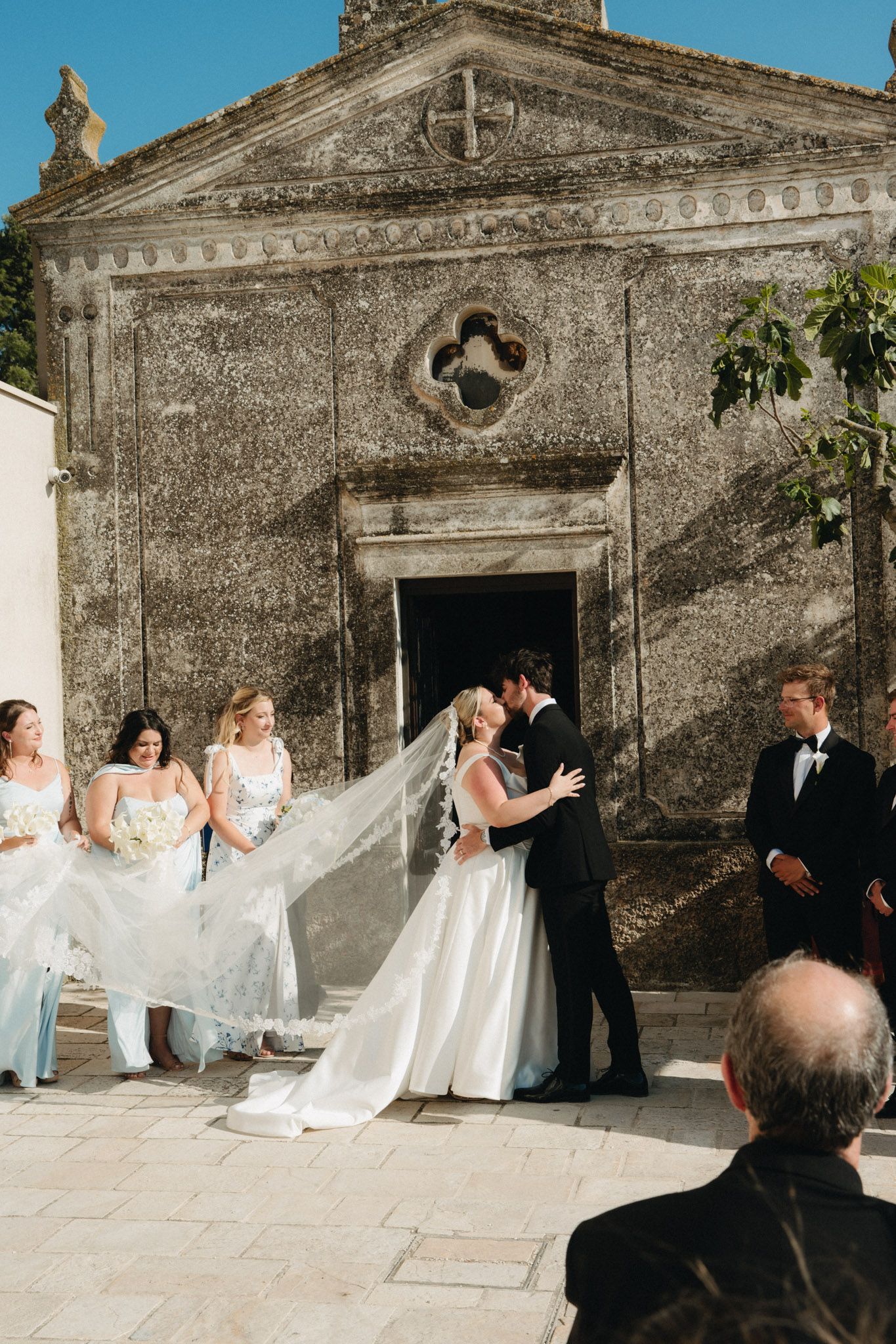 Bride and groom share first kiss outside historic stone chapel located in Matera, Italy.