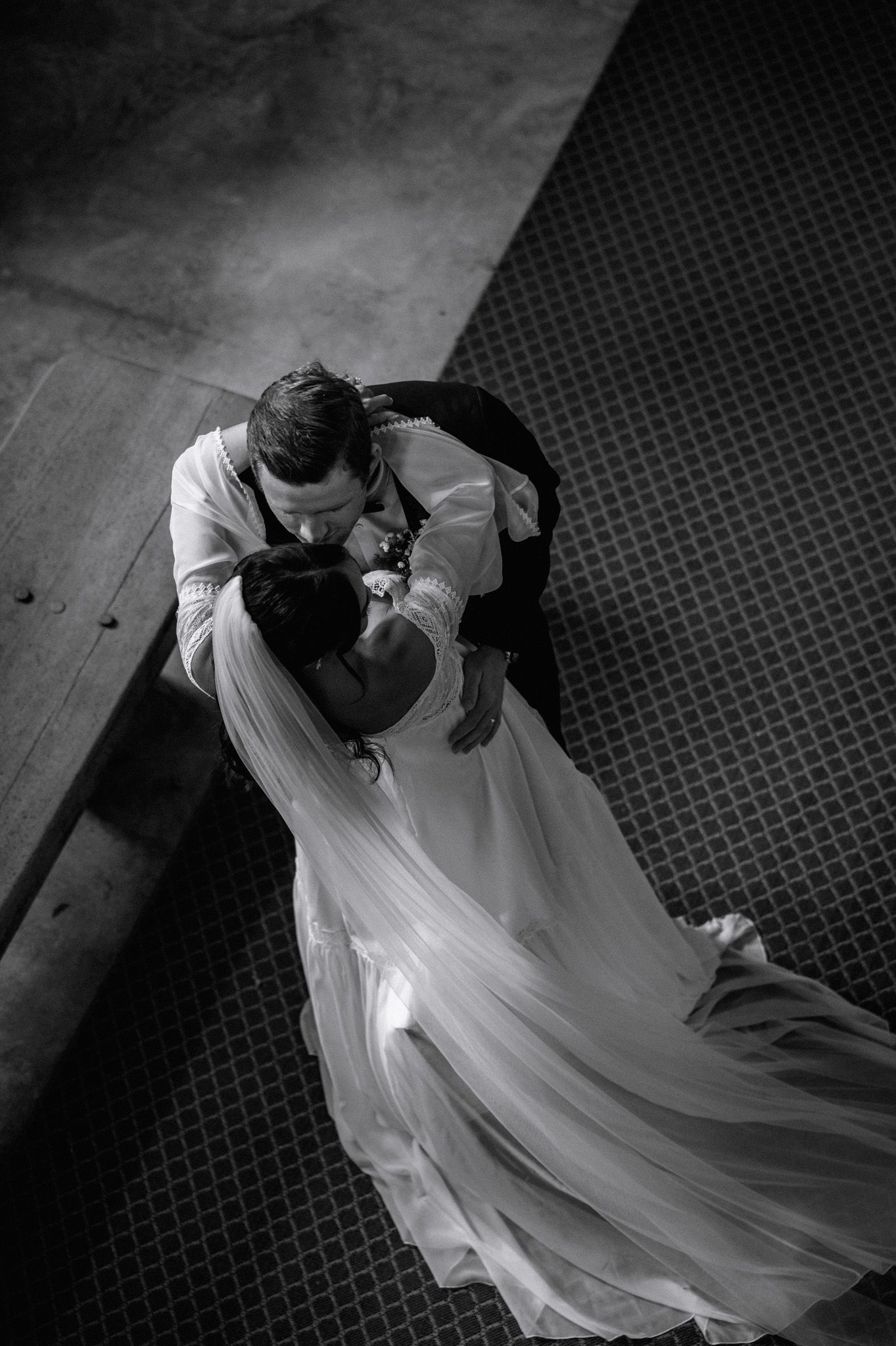 Black and white overhead shot of bride and groom sharing a tender embrace on a patterned floor inside a church.