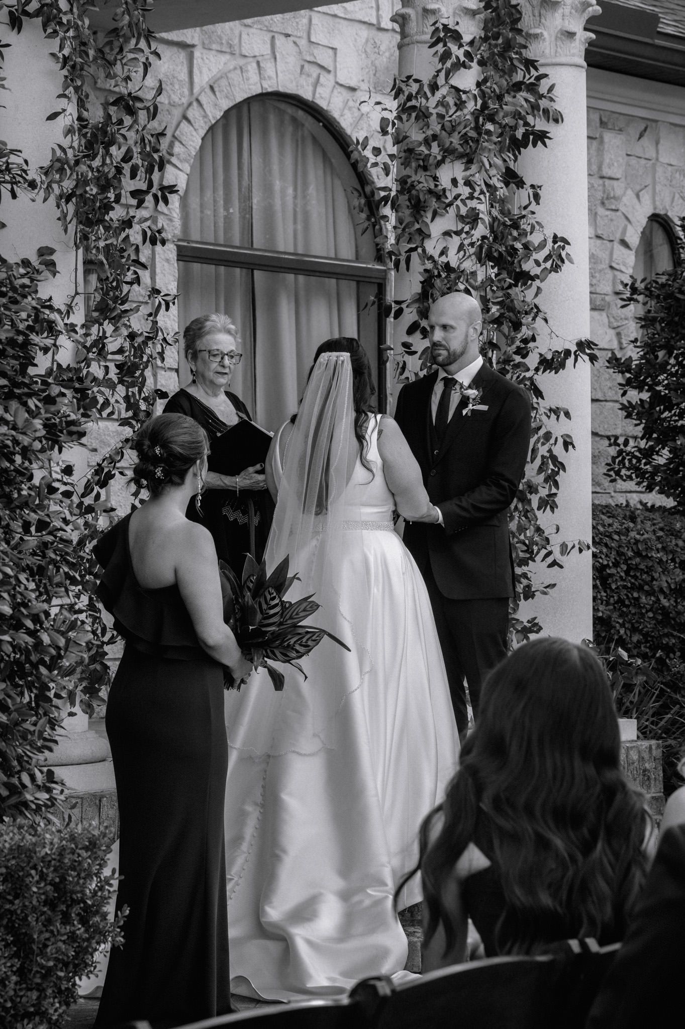 Bride and groom exchange vows at outdoor ceremony in black and white.