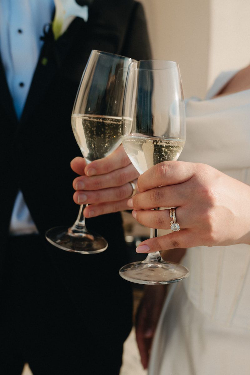 Bride and groom clinking champagne glasses in a wedding toast, bride wearing diamond engagement ring.
