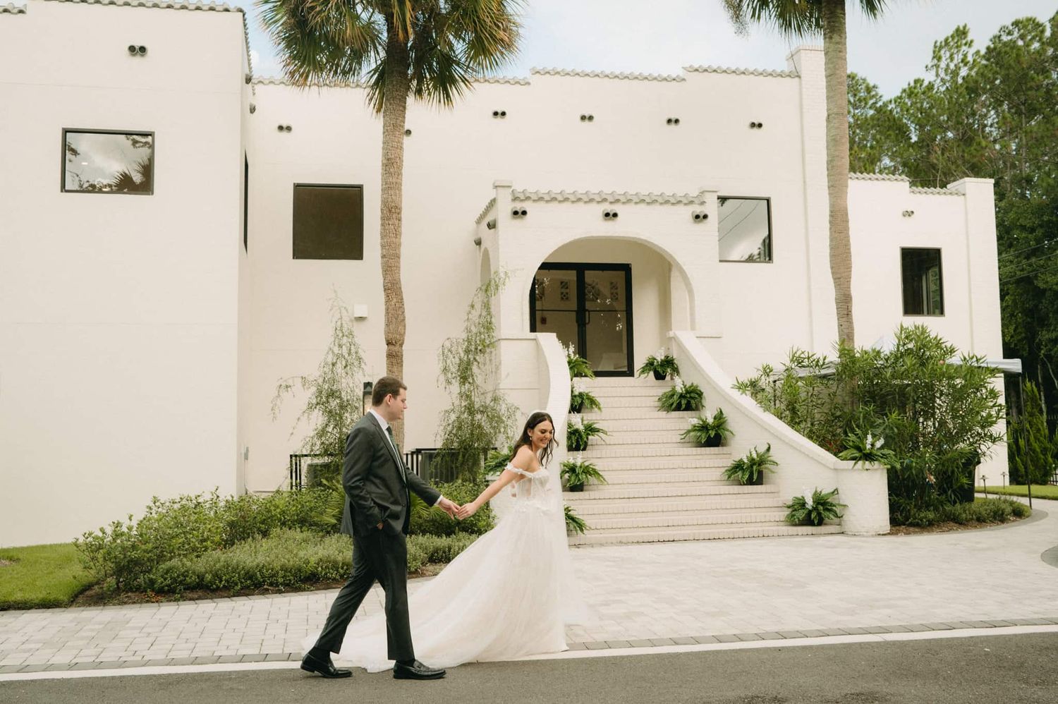 Bride and groom hold hands walking before white Spanish-style wedding venue in St. Augustine, FL.