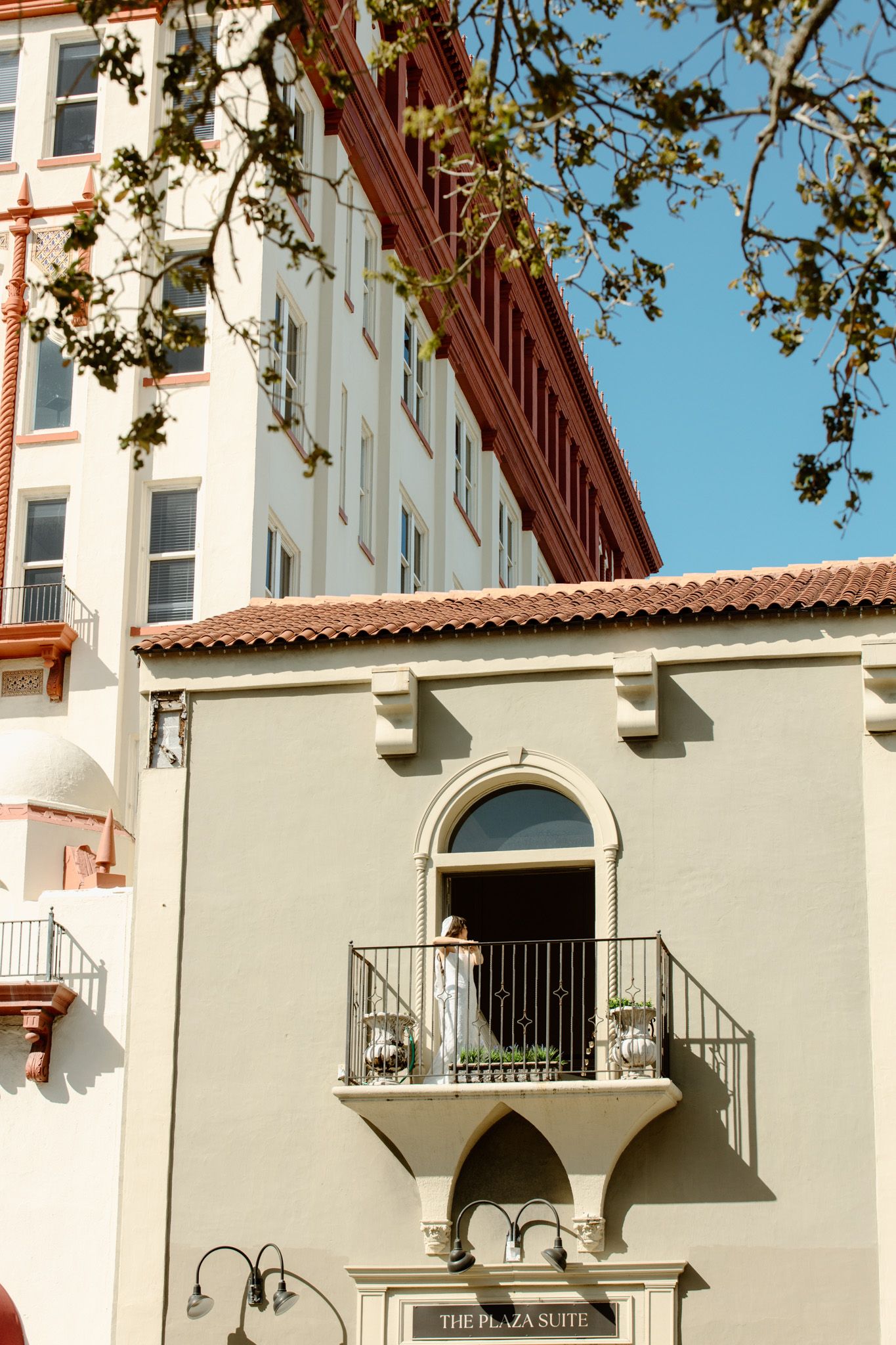 Bride stands on ornate balcony of The Plaza Suite building in historic St. Augustine, Florida on wedding day.