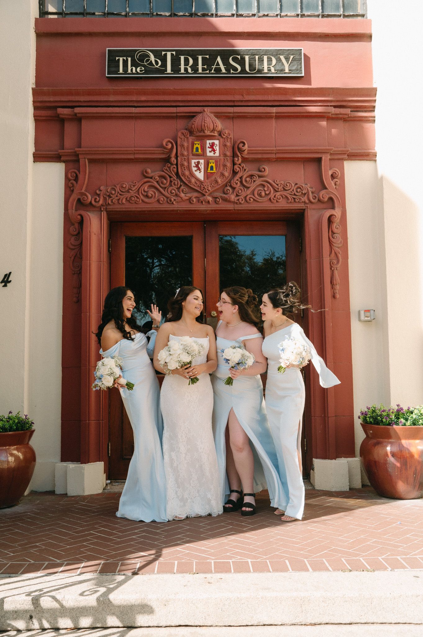 Bride and three bridesmaids in light blue gowns holding white bouquets outside The Treasury venue.