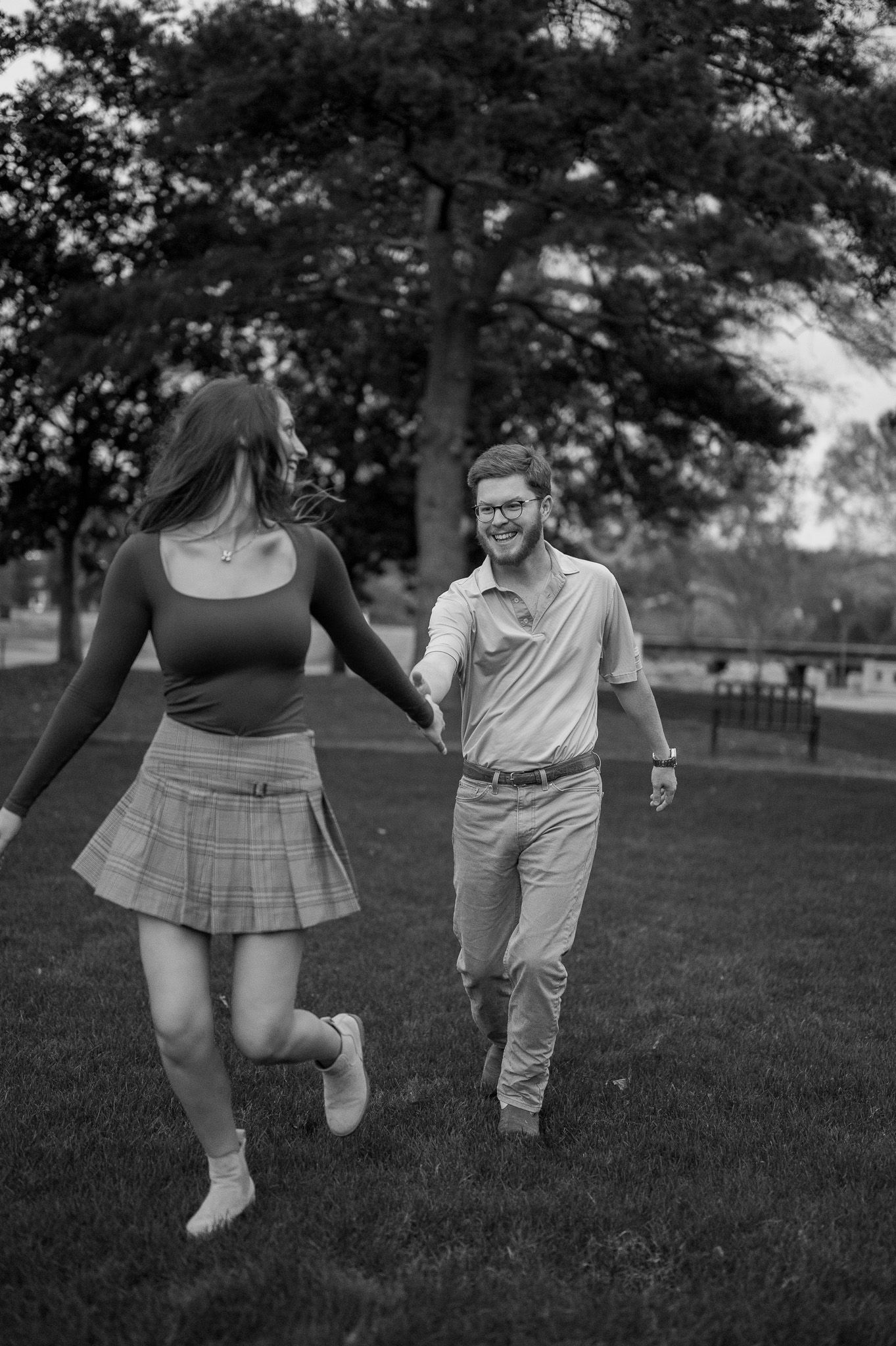 Black and white photo of a laughing couple running hand in hand across a park.