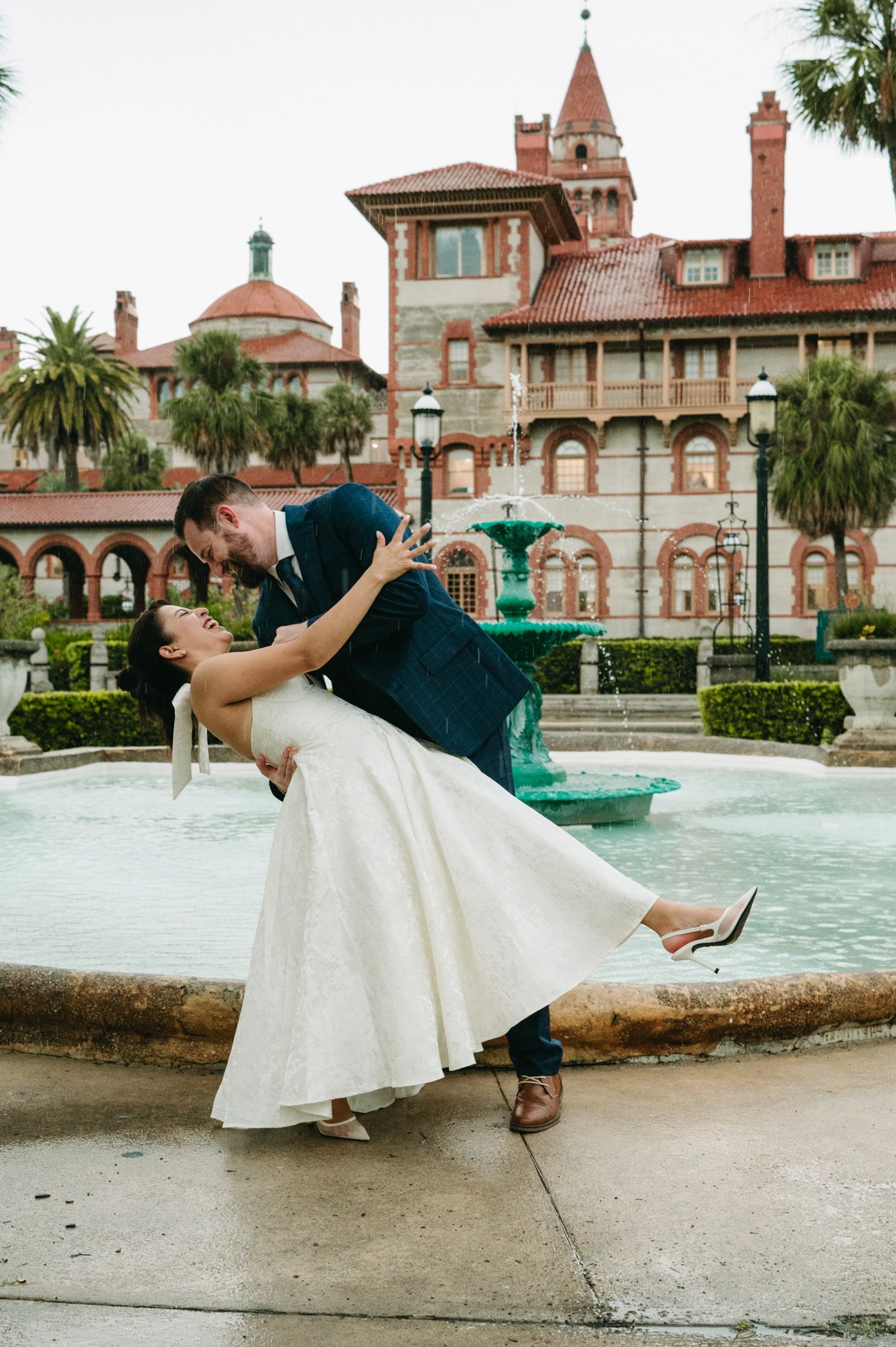 Groom dipping bride near fountain with historic Flagler College building in background.