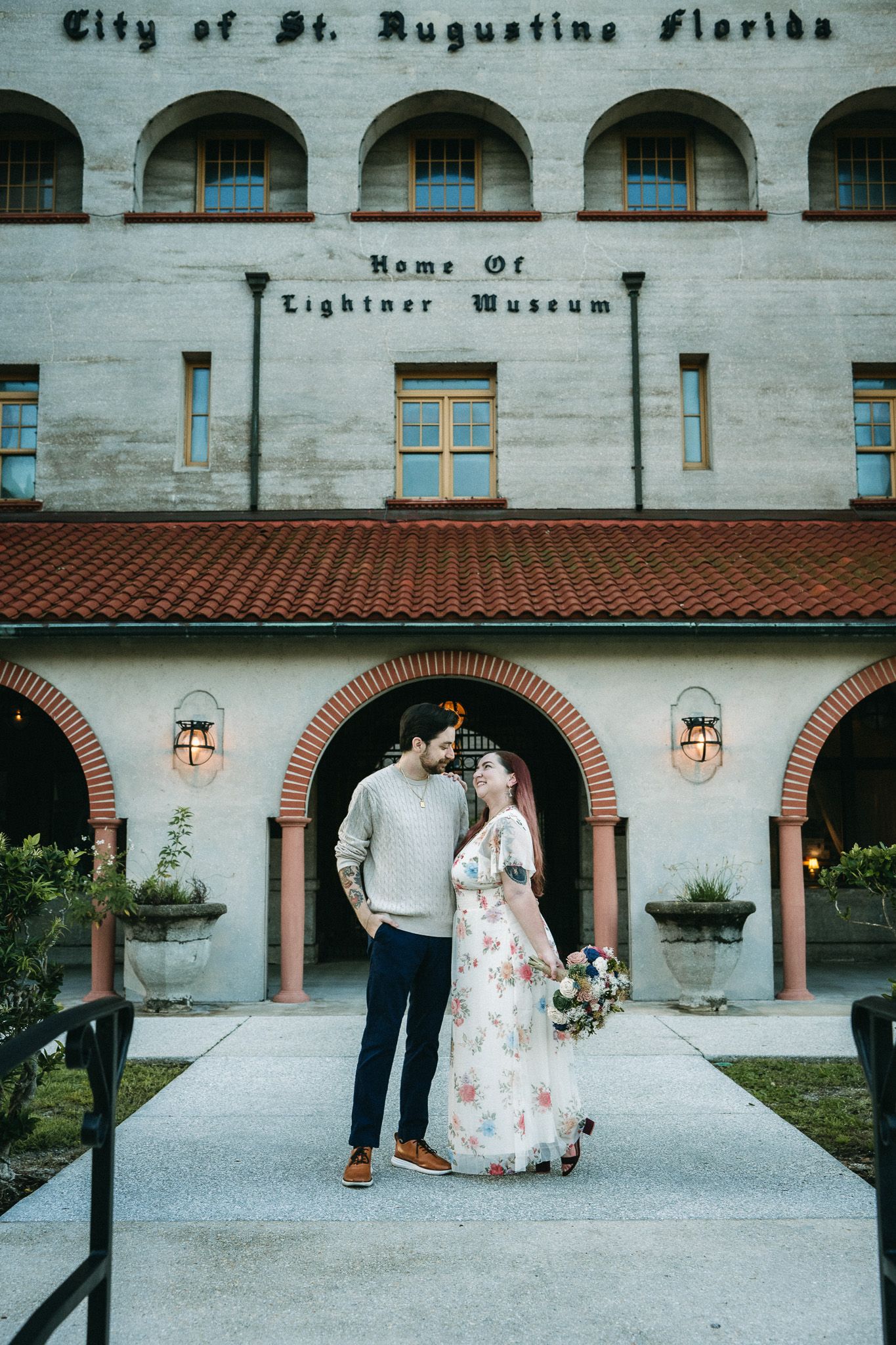Couple posing in front of the Lightner Museum in St. Augustine, Florida, bride holding floral bouquet in white dress.