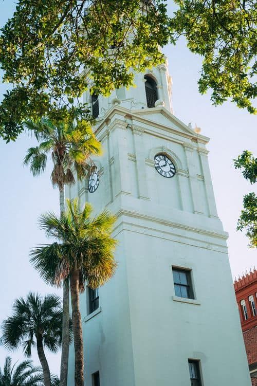 White historic clock tower with palm trees in St. Augustine, Florida against a blue sky.