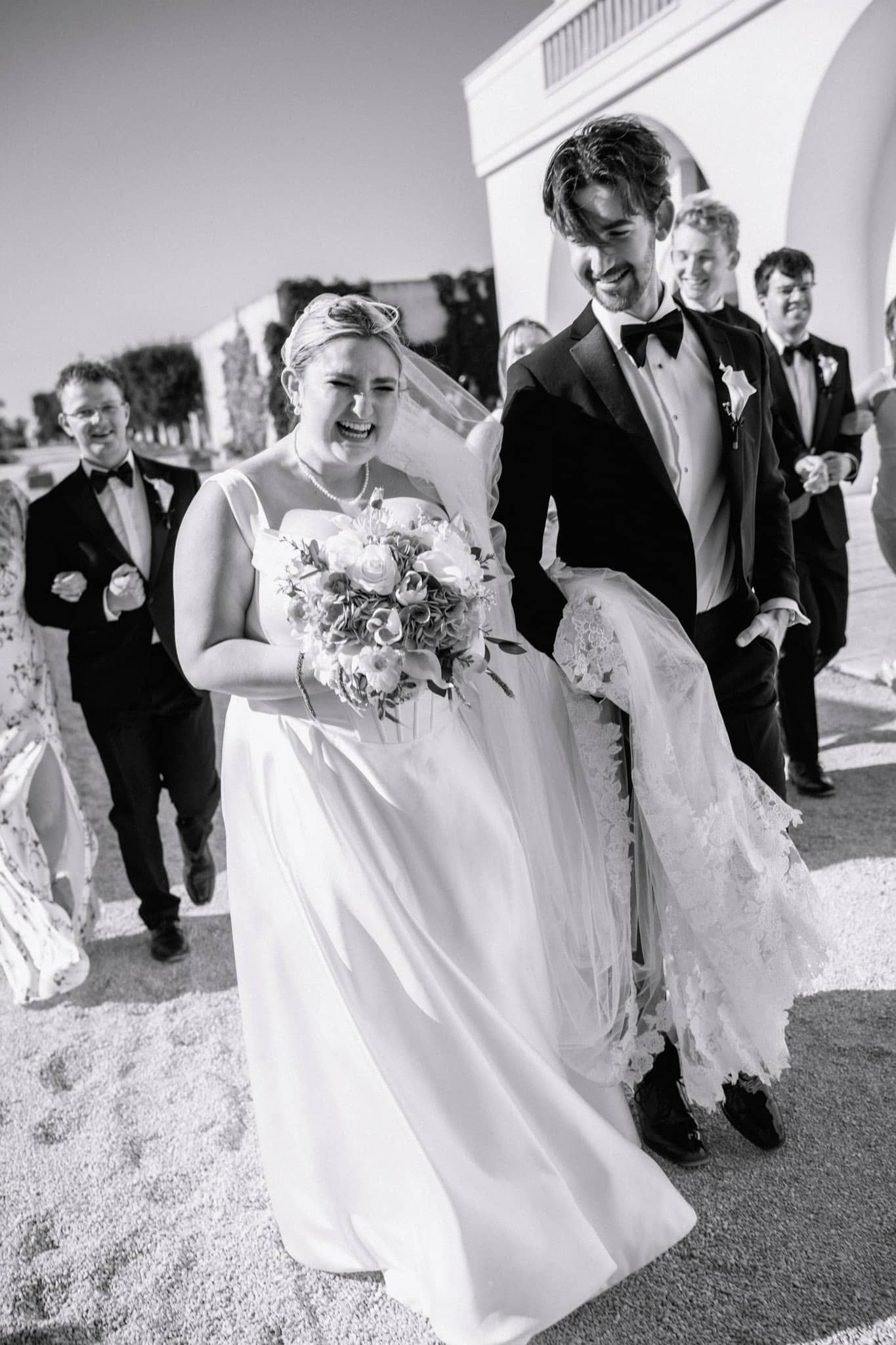 Black and white photo of a joyful bride and groom walking with groomsmen after their wedding ceremony in St. Augustine, FL.