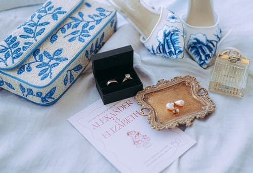 Wedding flat lay with engagement ring, invitation, blue embroidered purse, and bridal accessories.