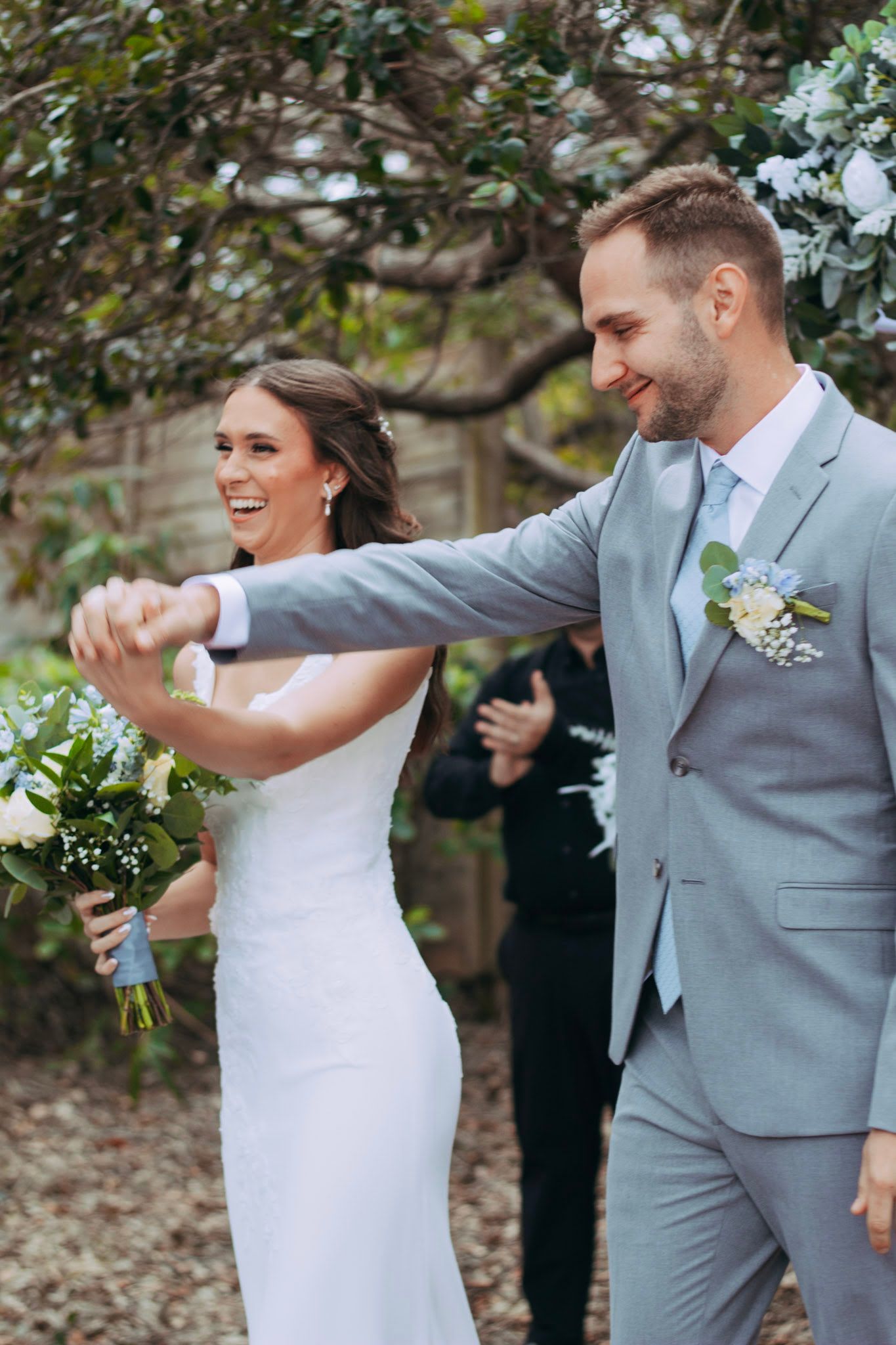 Joyful newlyweds celebrating after wedding ceremony, bride in white gown holding bouquet with groom in gray suit.