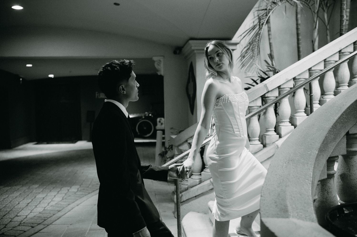 Black and white photo of bride and groom near ornate staircase at elegant wedding venue.