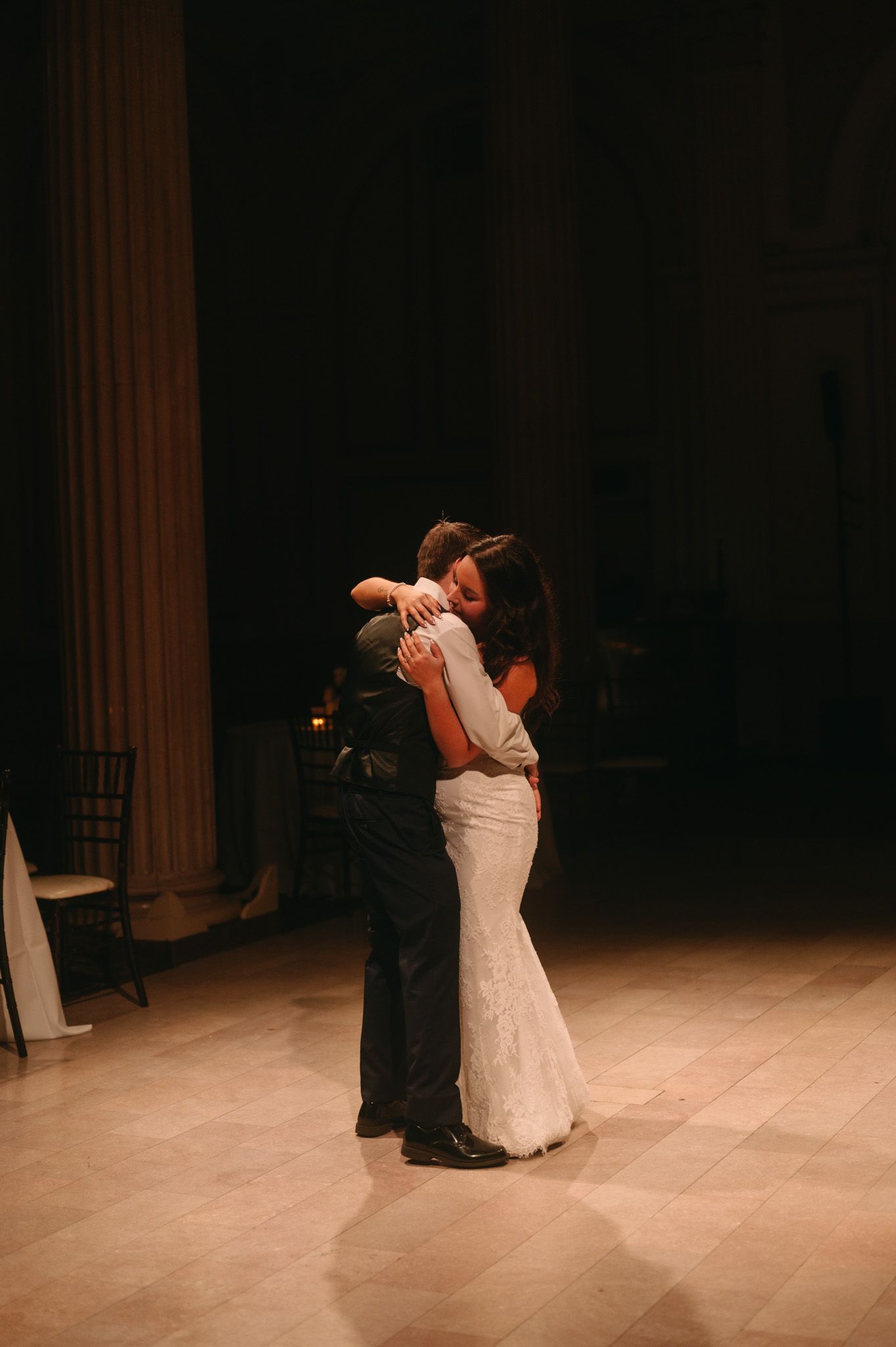 Bride and groom share an intimate first dance embrace in a dimly lit elegant ballroom during their wedding reception.