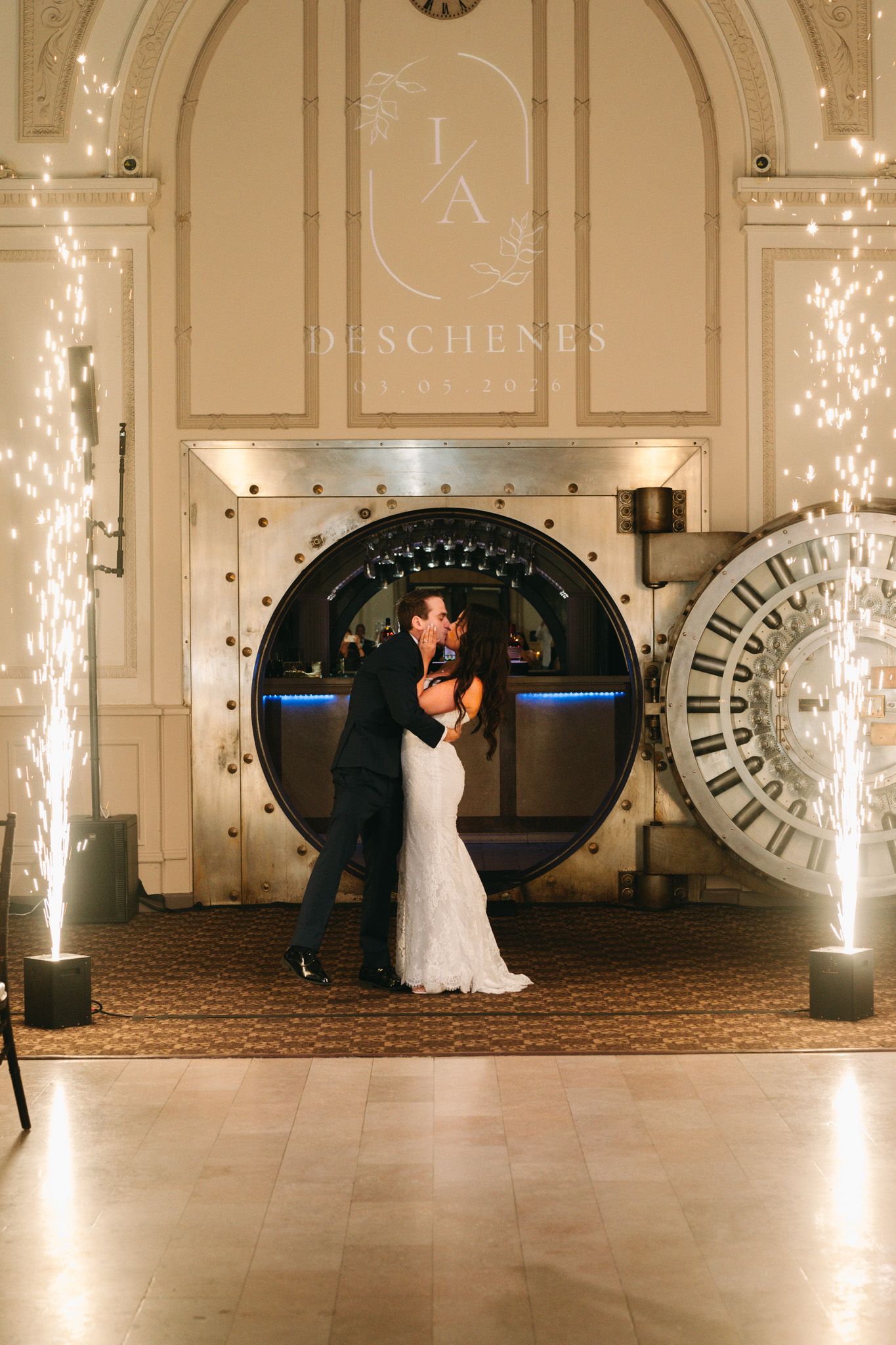 Bride and groom share first dance before a grand vault door with sparkling cold pyrotechnics at elegant wedding reception.