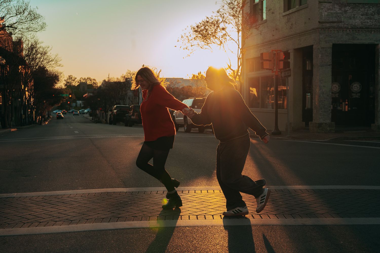 Couple holding hands crossing a sun-drenched street at golden hour in the city.