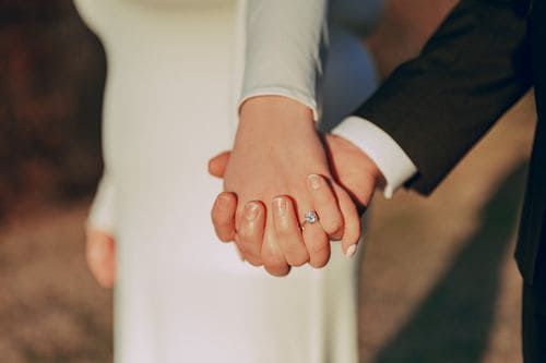 Close-up of newlyweds holding hands, bride wearing a diamond engagement and wedding ring.