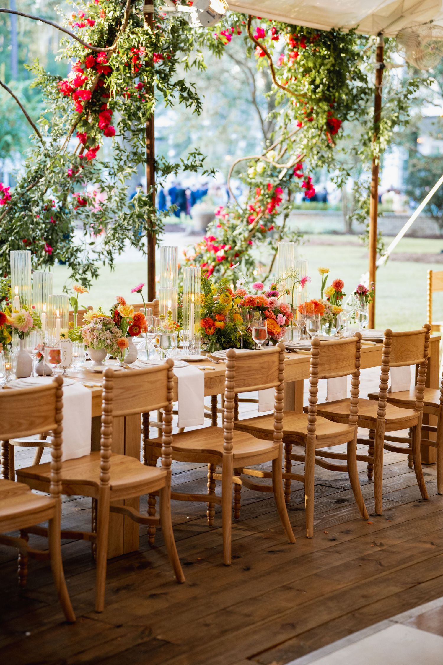 Rustic wooden chairs line a covered outdoor venue decorated with hanging red flowers and greenery for an elegant event setup.