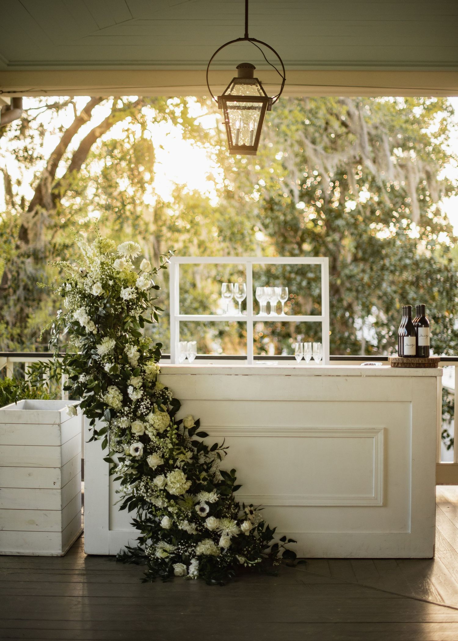 Elegant white wedding bar setup with floral arrangements and lanterns in an outdoor covered venue.