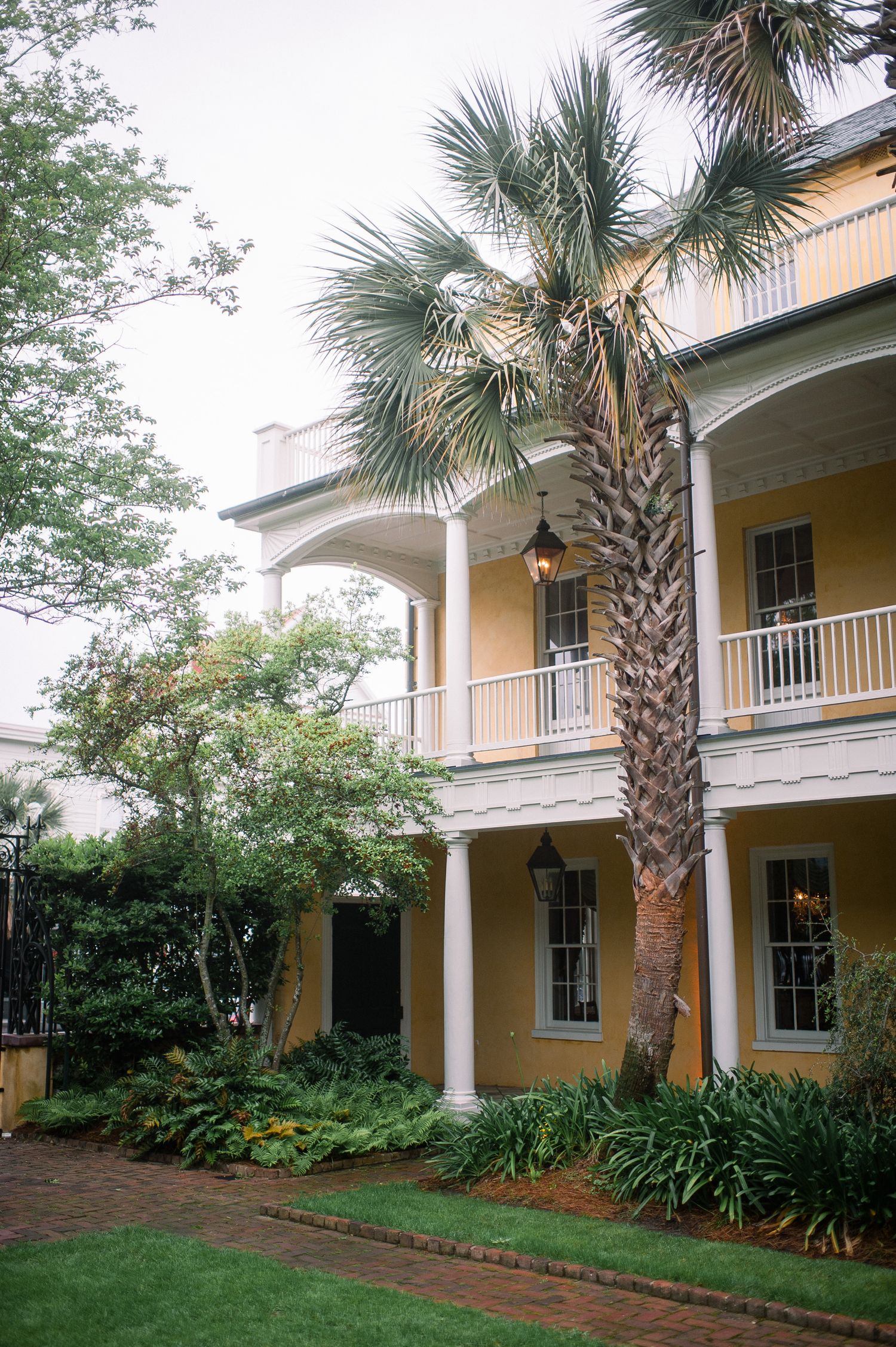 Colonial-style yellow building with white columns and palm trees along a landscaped walkway.