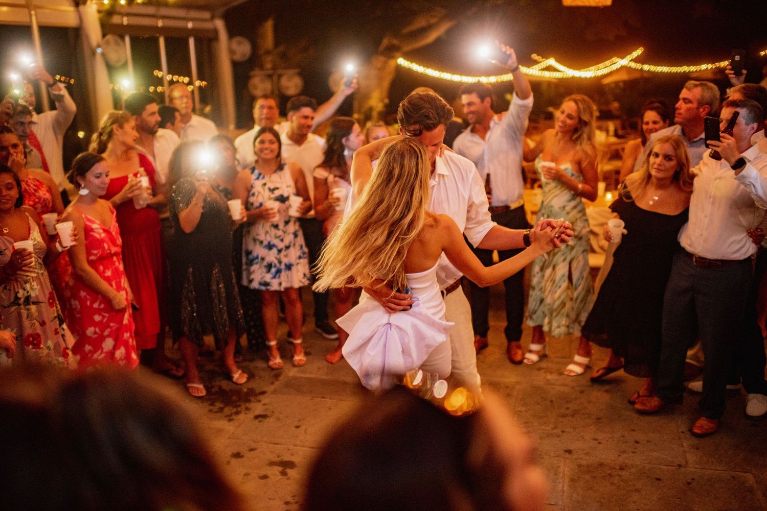 A lively crowd dances together at a festive evening celebration with warm lighting and joyful atmosphere.