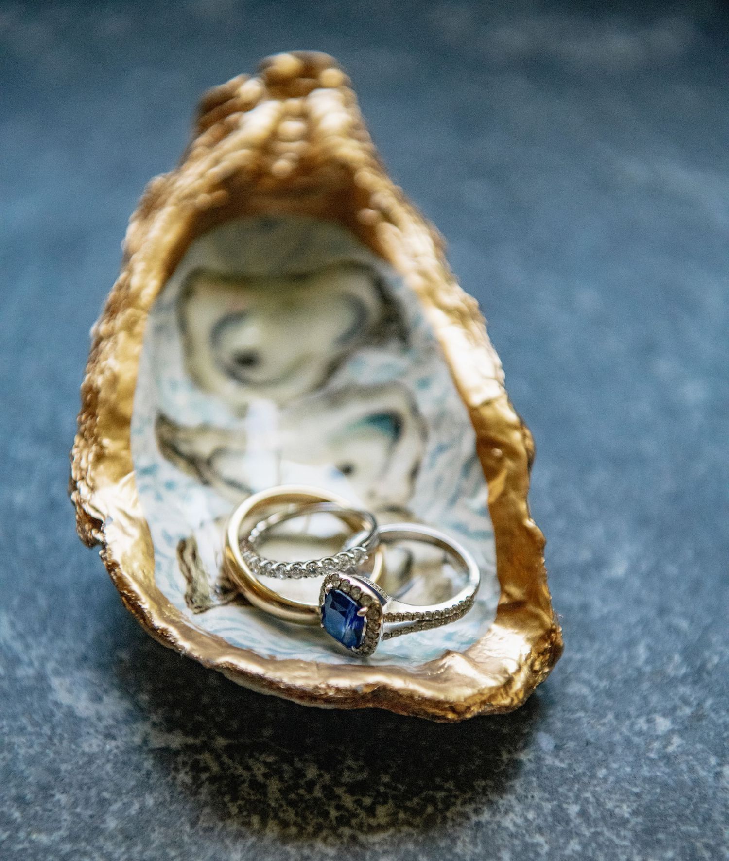 A delicate diamond engagement ring nestled inside a golden oyster shell on a dark surface.