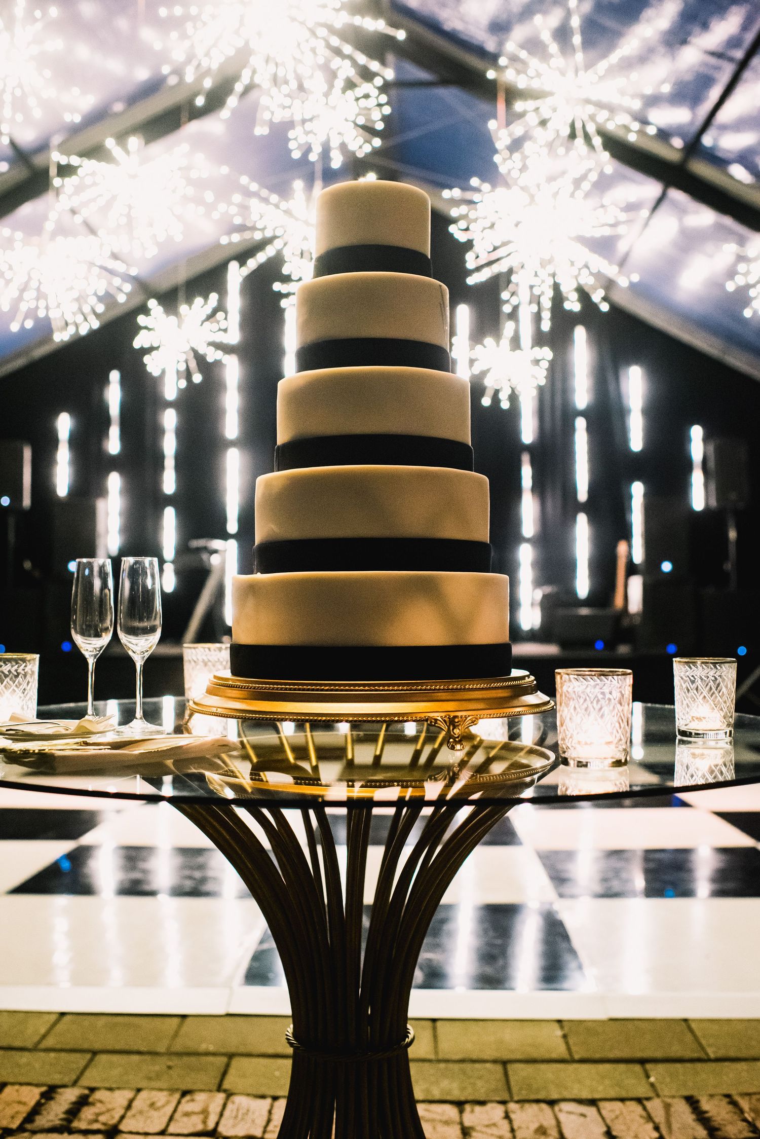Modern black and white tiered wedding cake displayed on a pedestal with glowing snowflake decorations in the background.