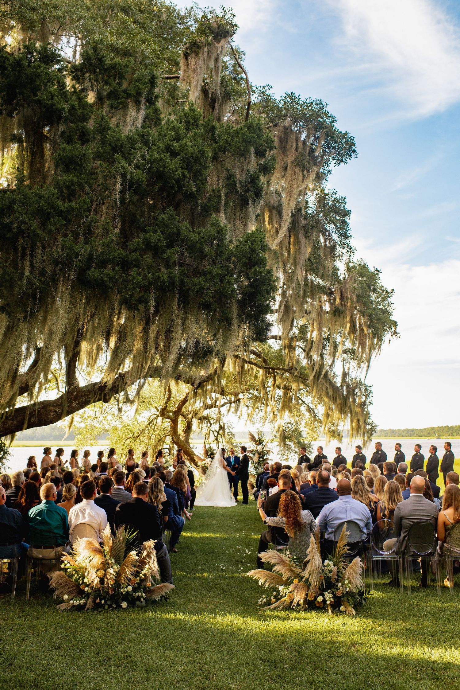 Outdoor wedding ceremony under a majestic oak tree draped with Spanish moss at sunset.