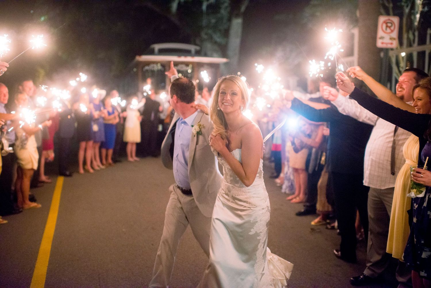 Newlyweds walk through a sparkler-lit pathway during their evening wedding exit celebration.