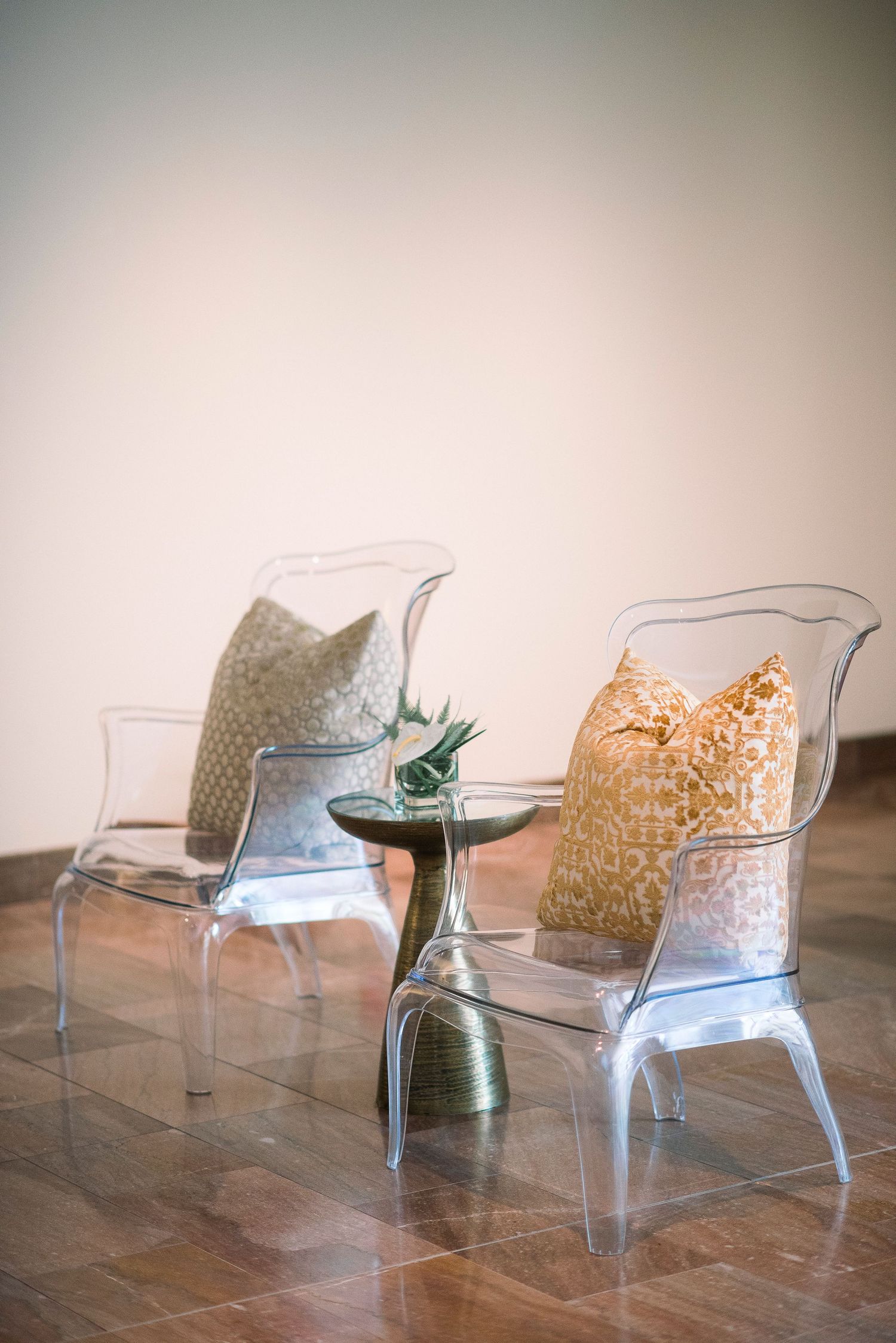 A transparent modern acrylic chair with a decorative pillow sits on a wooden floor in a minimalist setting.