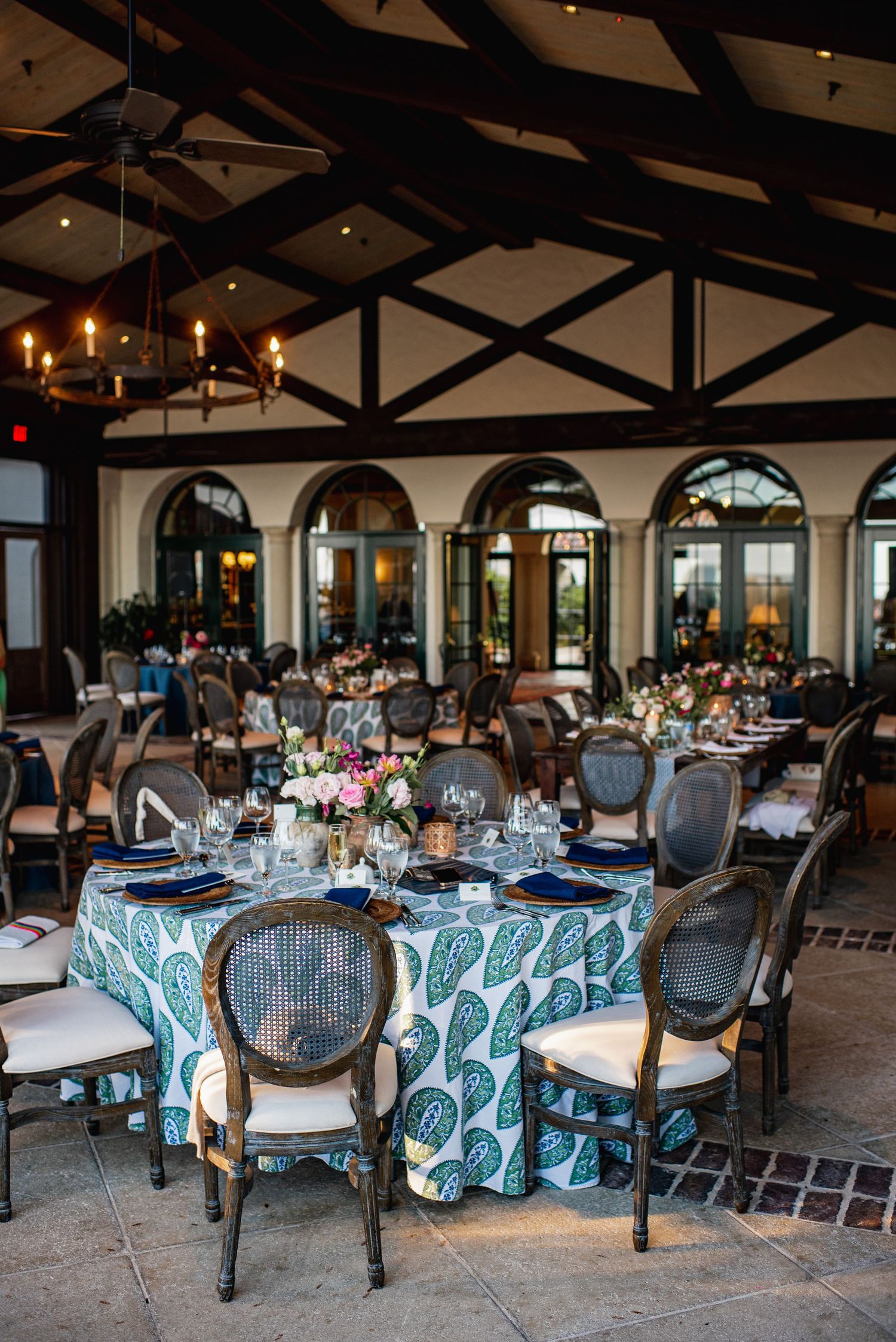 Wedding reception venue with elegant table settings featuring blue patterned tablecloths and cane back chairs.
