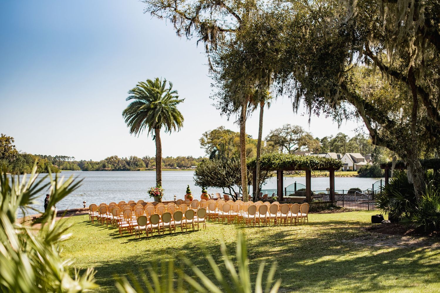 A panoramic view of a waterfront wedding ceremony setup with wooden chairs and Spanish moss draped trees in Florida.