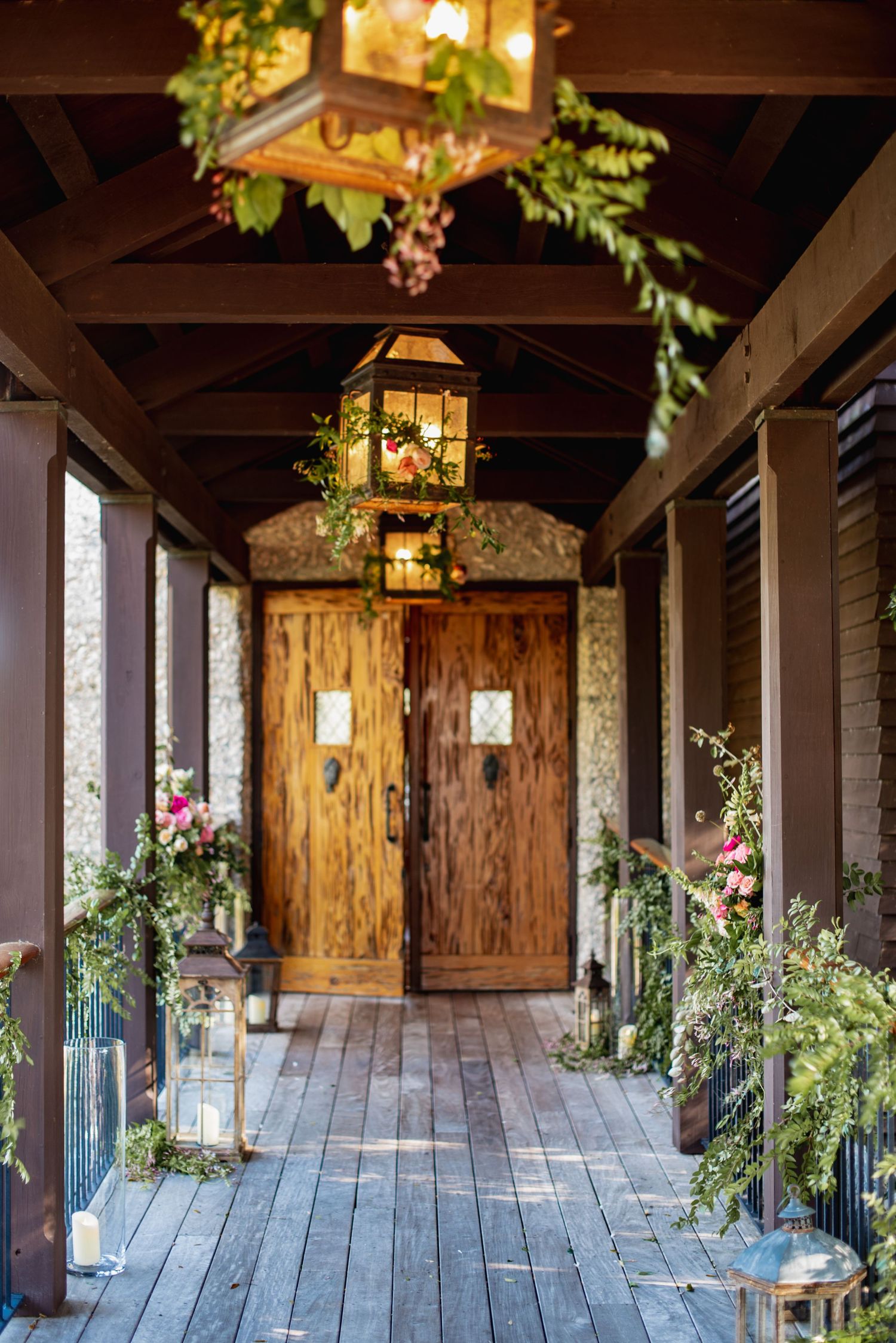 Rustic covered porch walkway with wooden beams, hanging lanterns and greenery decorations creating a romantic ambiance.