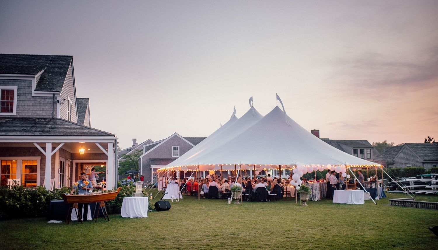 Elegant white tent wedding reception venue at dusk with guests arriving.