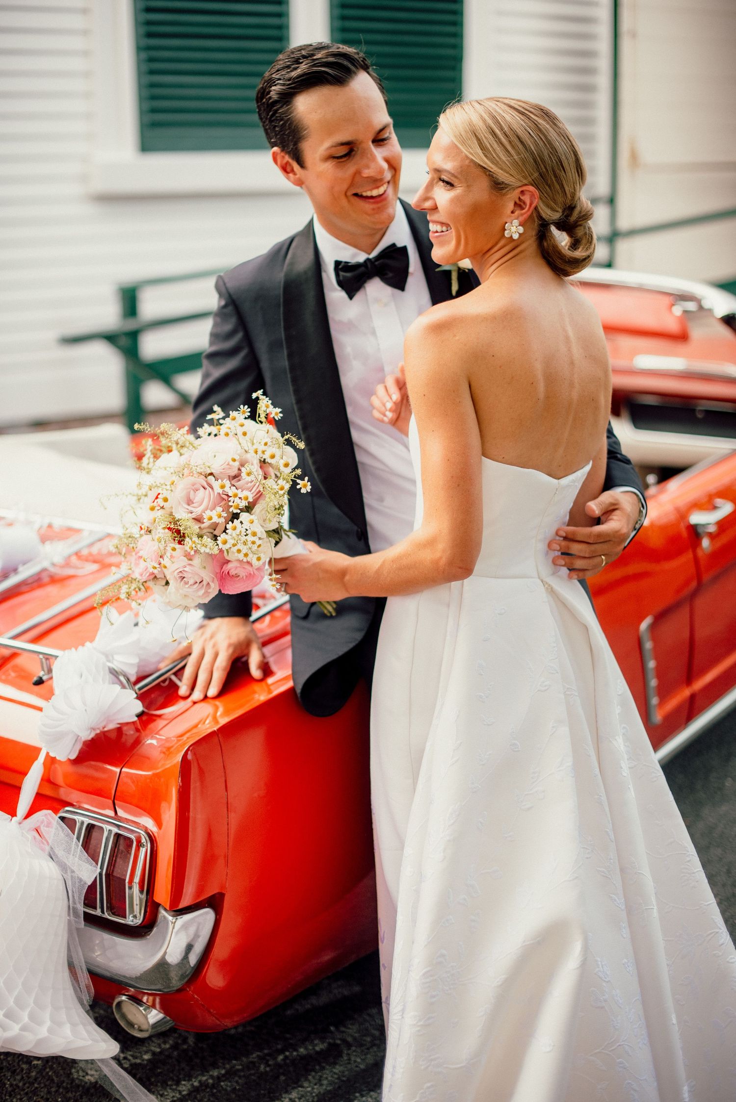 Newlyweds share intimate moments beside a vintage red car during their wedding photoshoot.