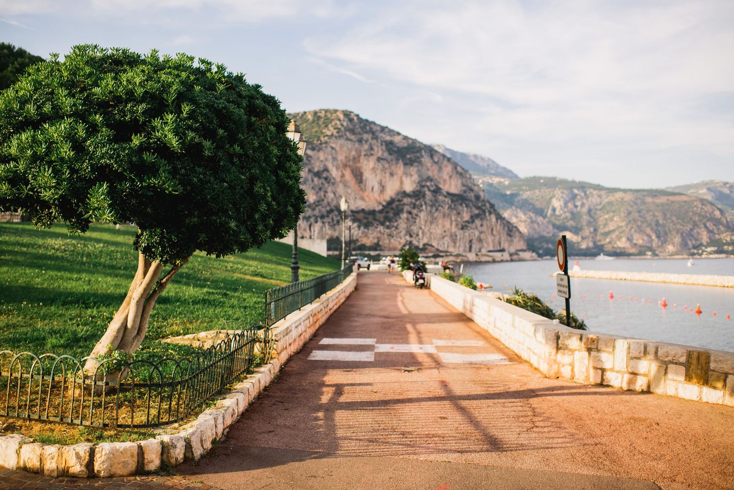 Scenic coastal promenade with palm trees and mountains overlooking the Mediterranean Sea.
