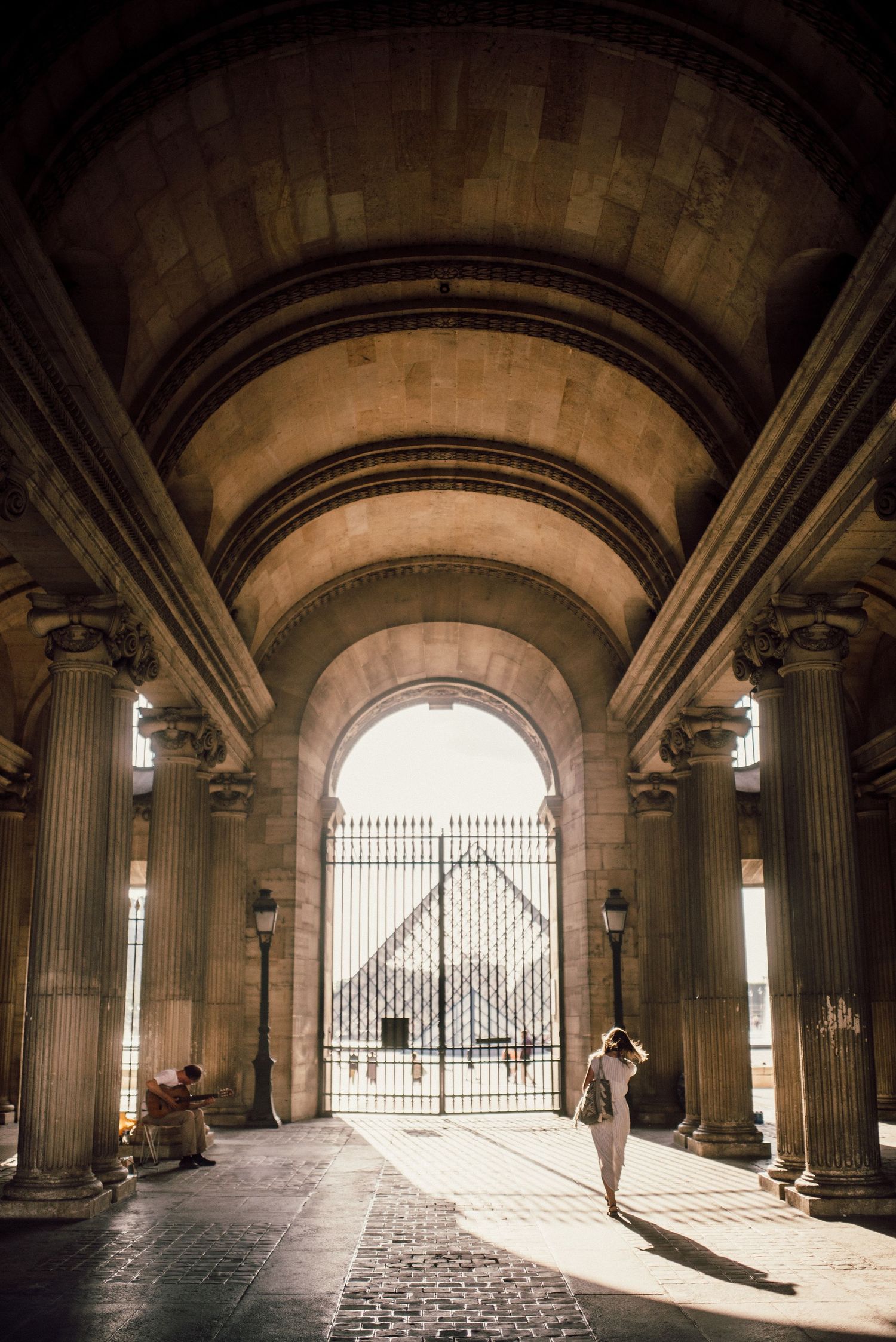 Stone archway corridor with dramatic sunlight streaming through iron gates creates architectural perspective.