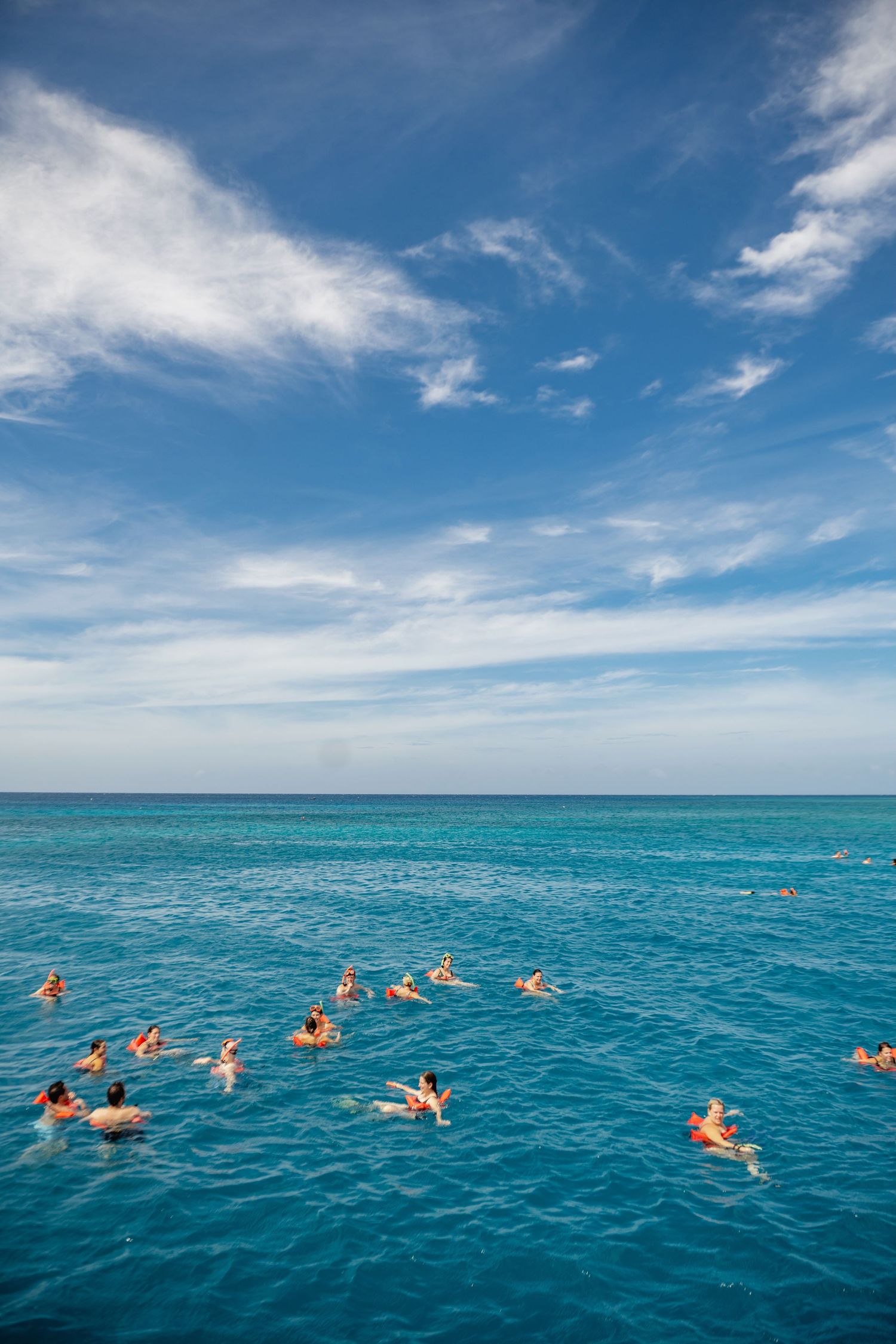 People floating in crystal clear turquoise waters of Jamaica under a bright blue sky with wispy clouds.