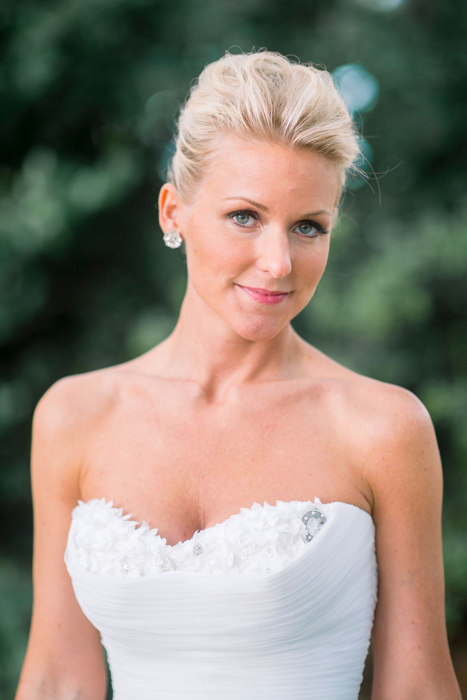 Elegant bride in white strapless wedding dress with sweetheart neckline and lace details poses outdoors.