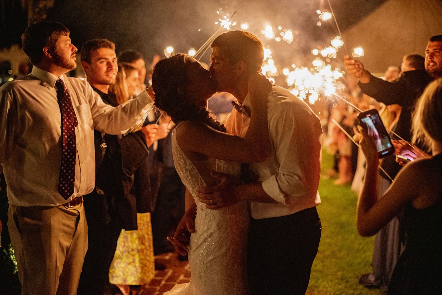 Wedding guests hold sparklers creating a magical nighttime celebration atmosphere at an outdoor reception.